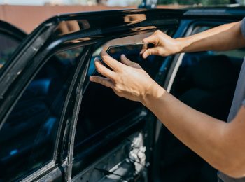 A man is changing a side window of his car outdoors.