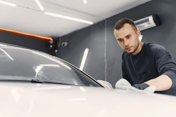 Man in a garage. Worker polish a car. Man in a black uniform.